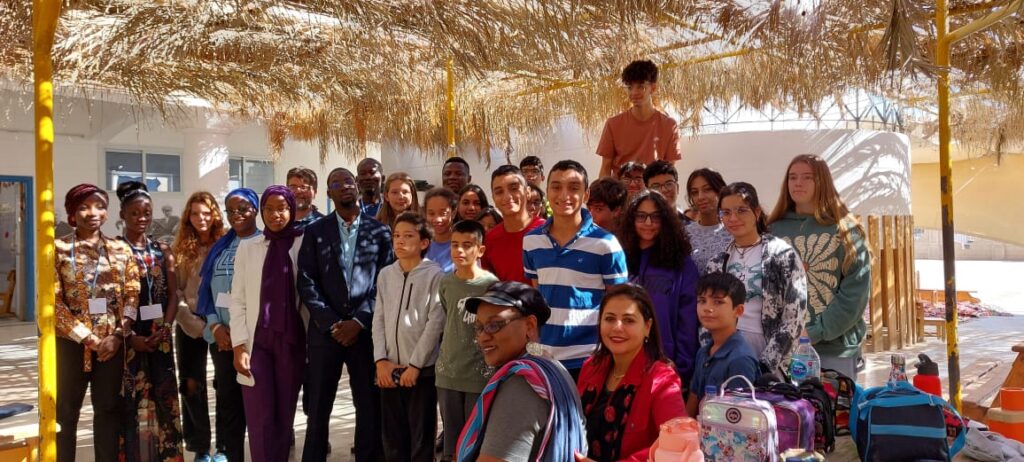 A diverse group of students and faculty members posing for a photo under a thatched roof at the French school in Sharm El Sheikh.